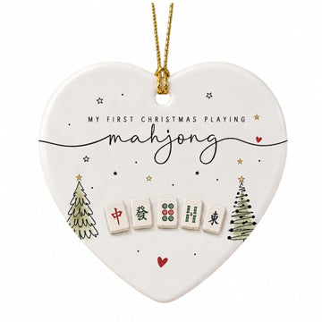 White heart-shaped ceramic ornament with two small Christmas trees, mahjong tiles and the words My First Christmas Playing mahjong